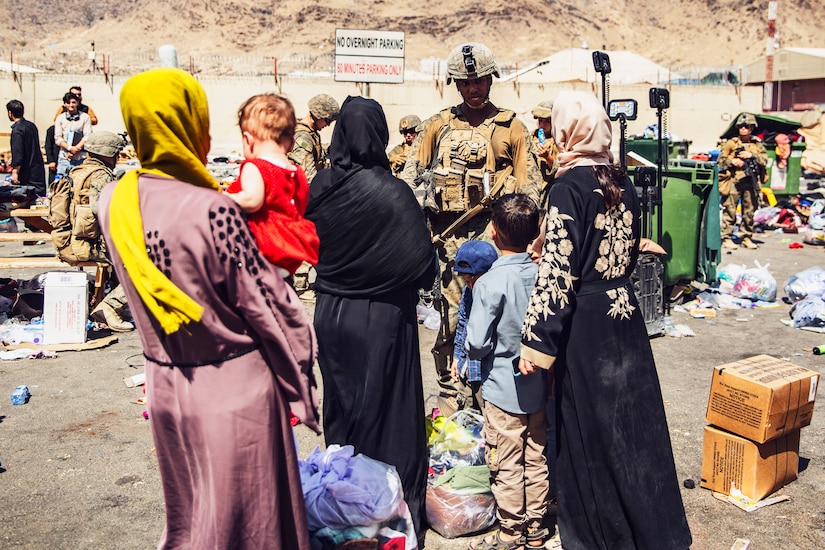 A Marine faces a group of civilians with others in the background.