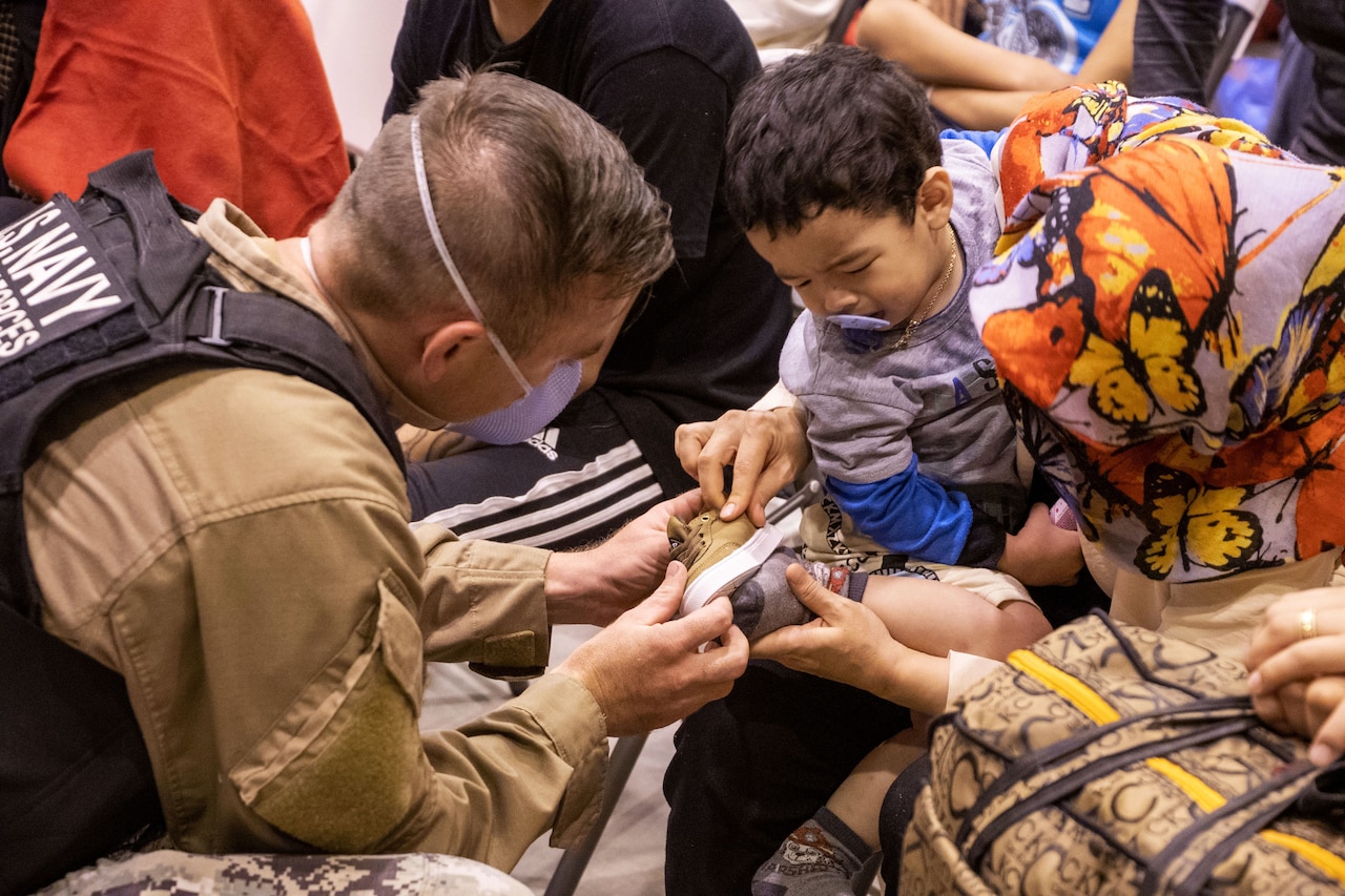 A sailor fits a shoe onto a child being held by a civilian.