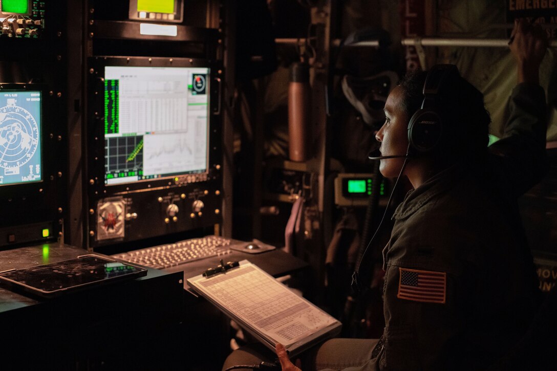 An airman wearing a headset looks at several screens.