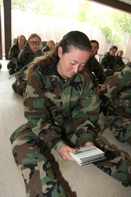 A girl in camouflaged outfit sits in line reading.