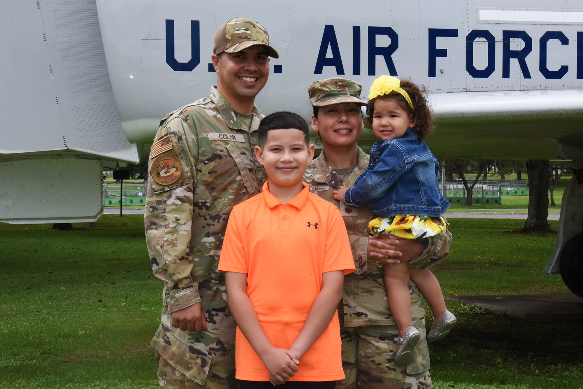 A military family stands in front of a jet.