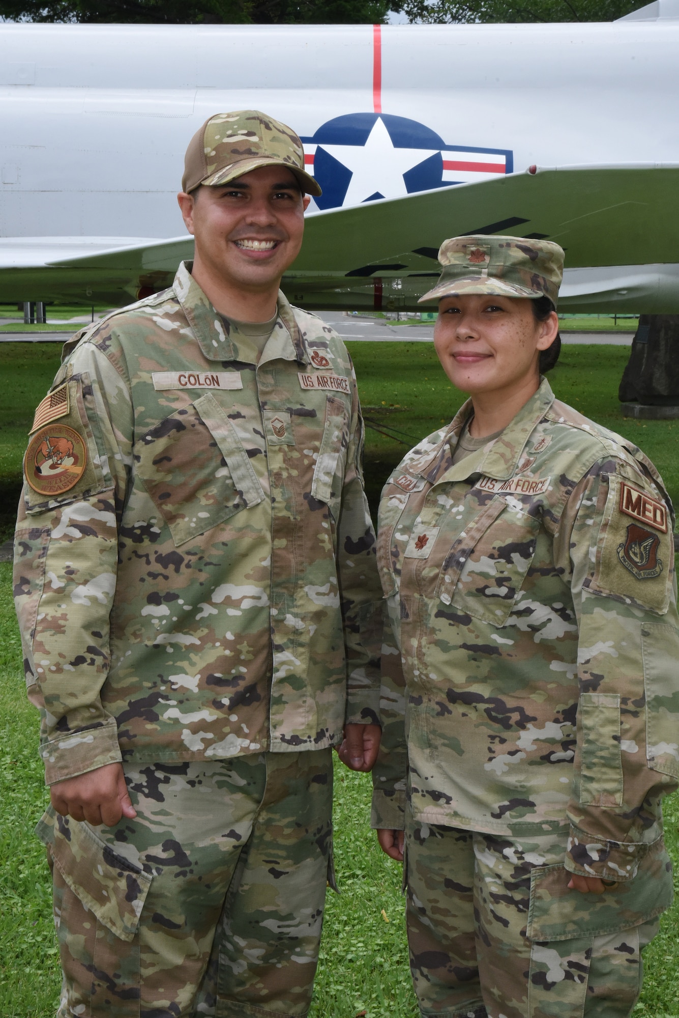 A man and a woman in uniform pose in front of a jet.