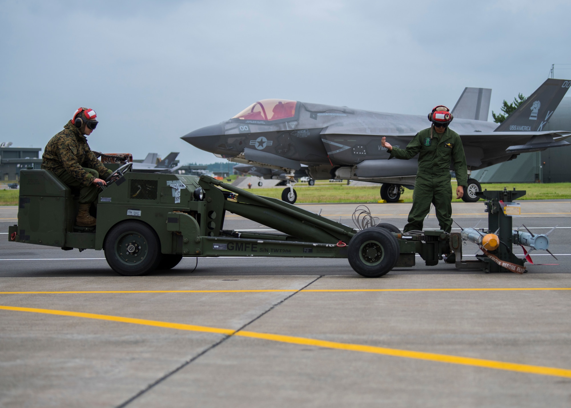 A person drives a weapon lifting machine while another stands nearby.
