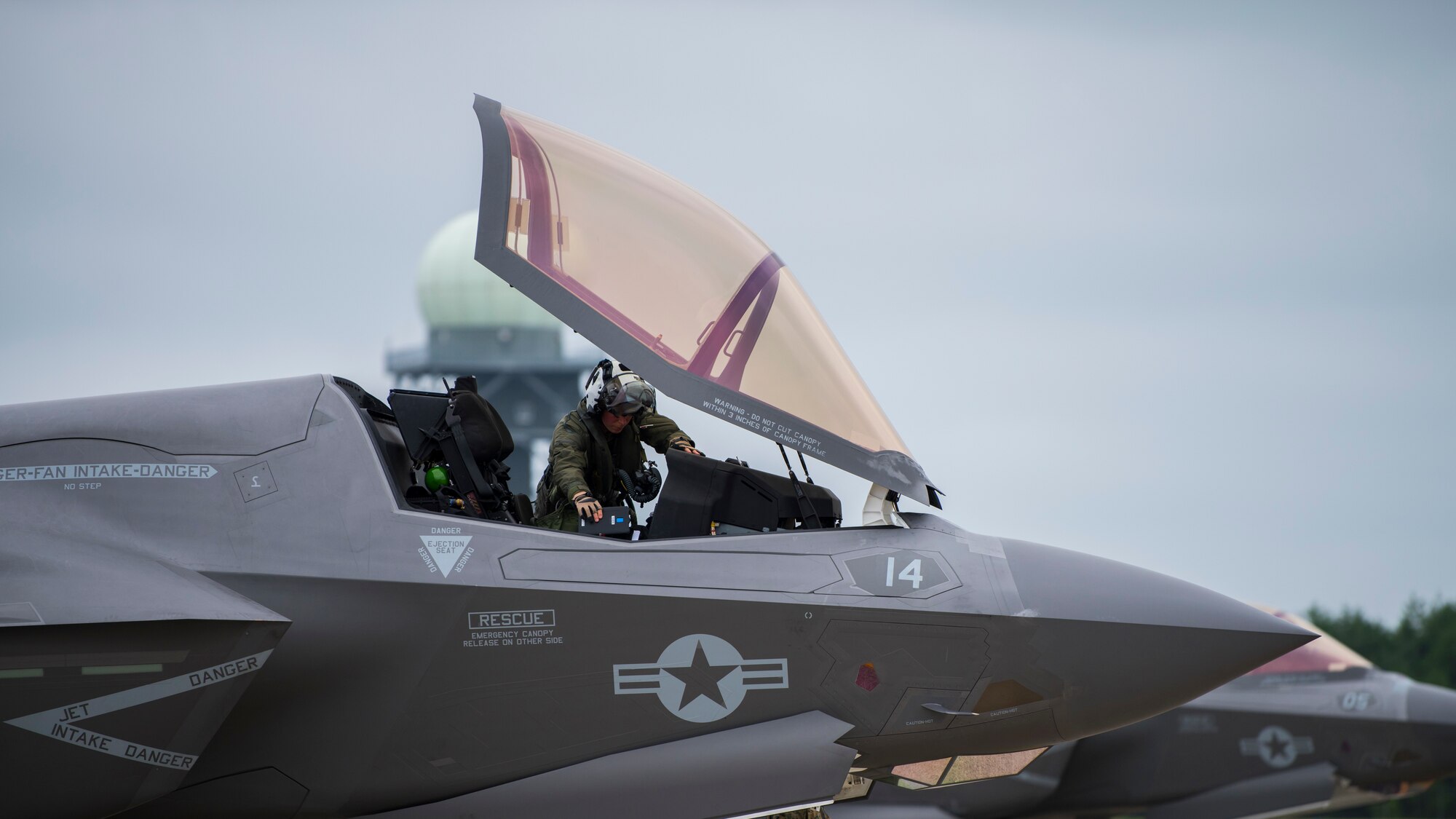 A person in uniform leans into an open canopy of an F-35 fighter  jet.