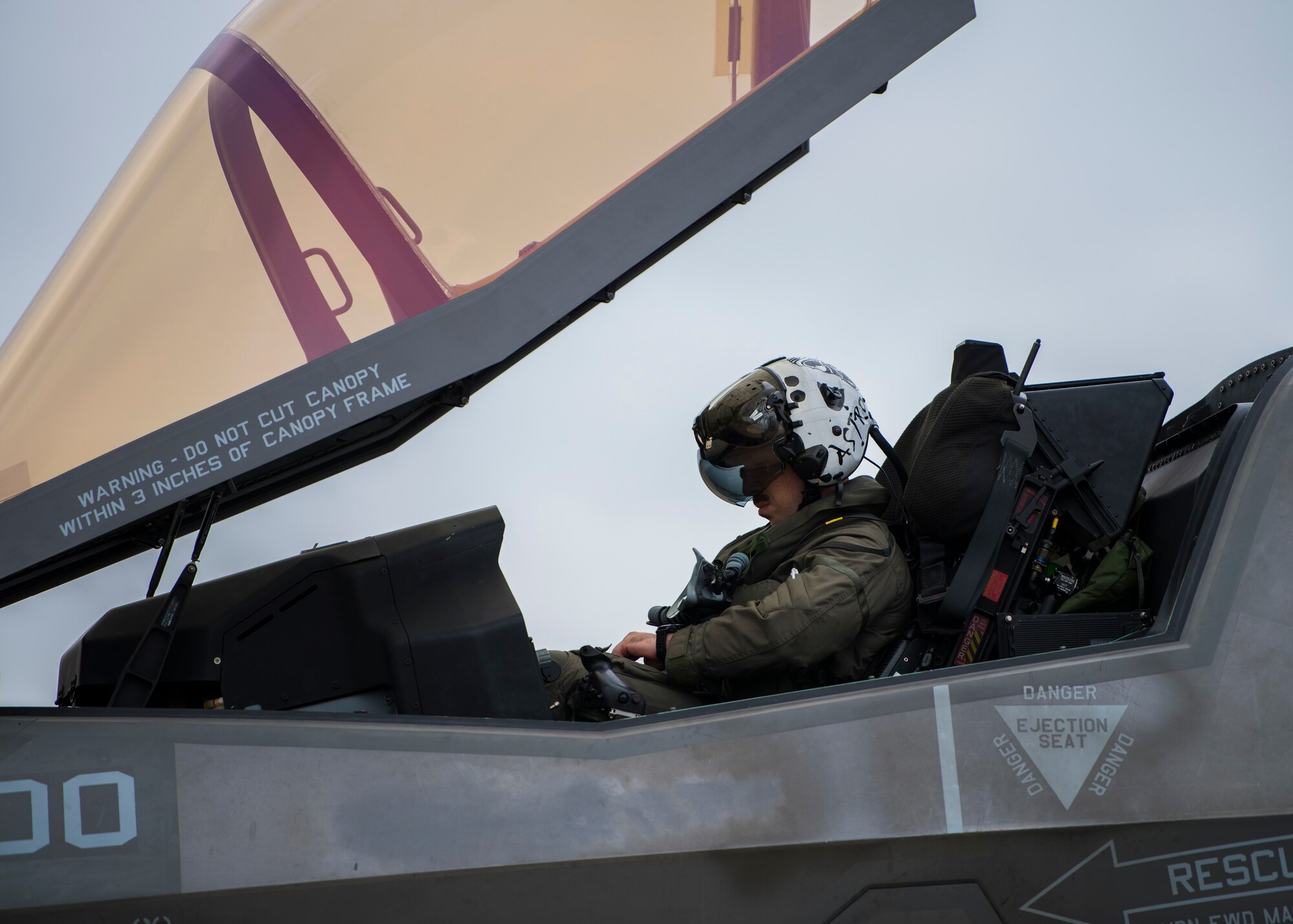 A pilot sits in the cockpit of an F-35. The canopy is open.