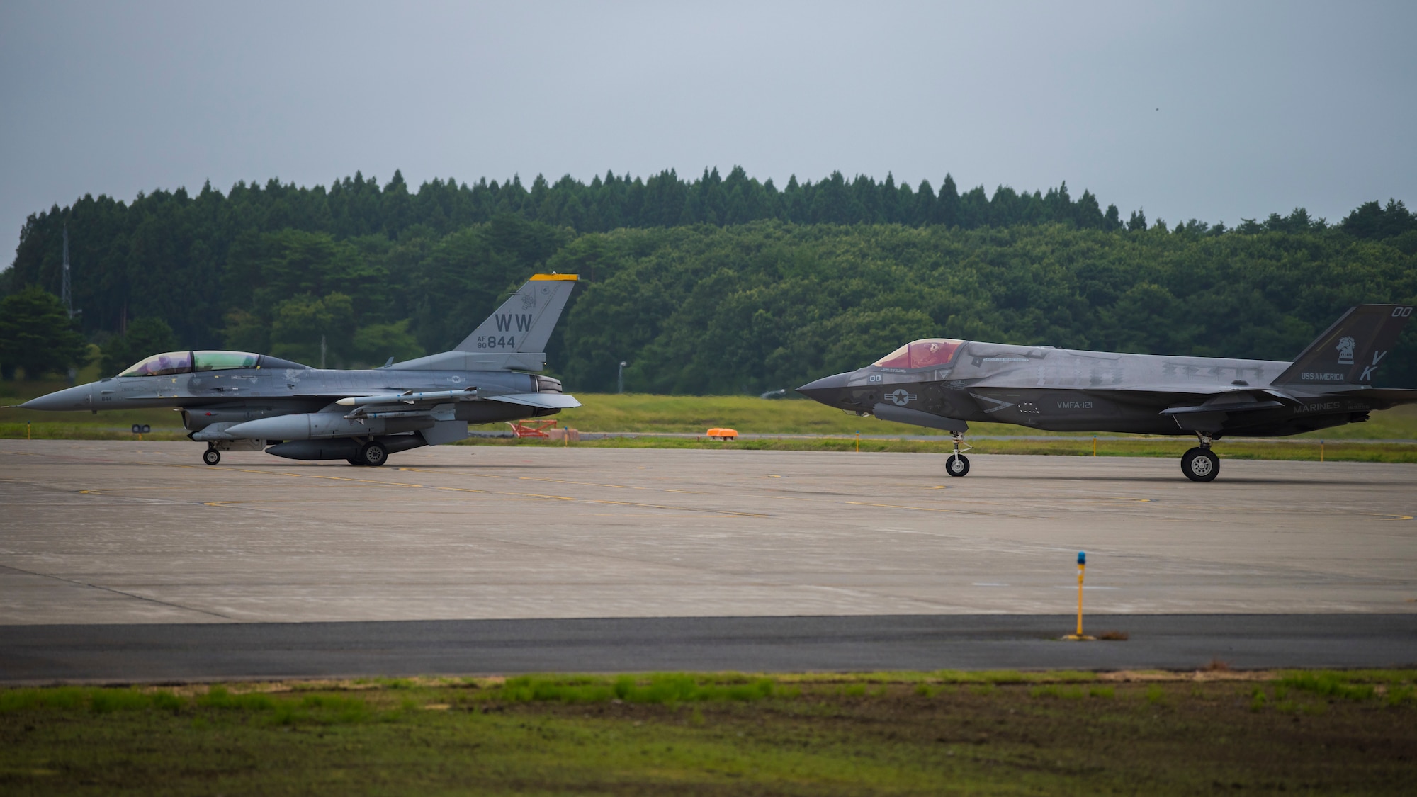 Two fighter jets, an F-16 followed by an F-35, taxi from the right.