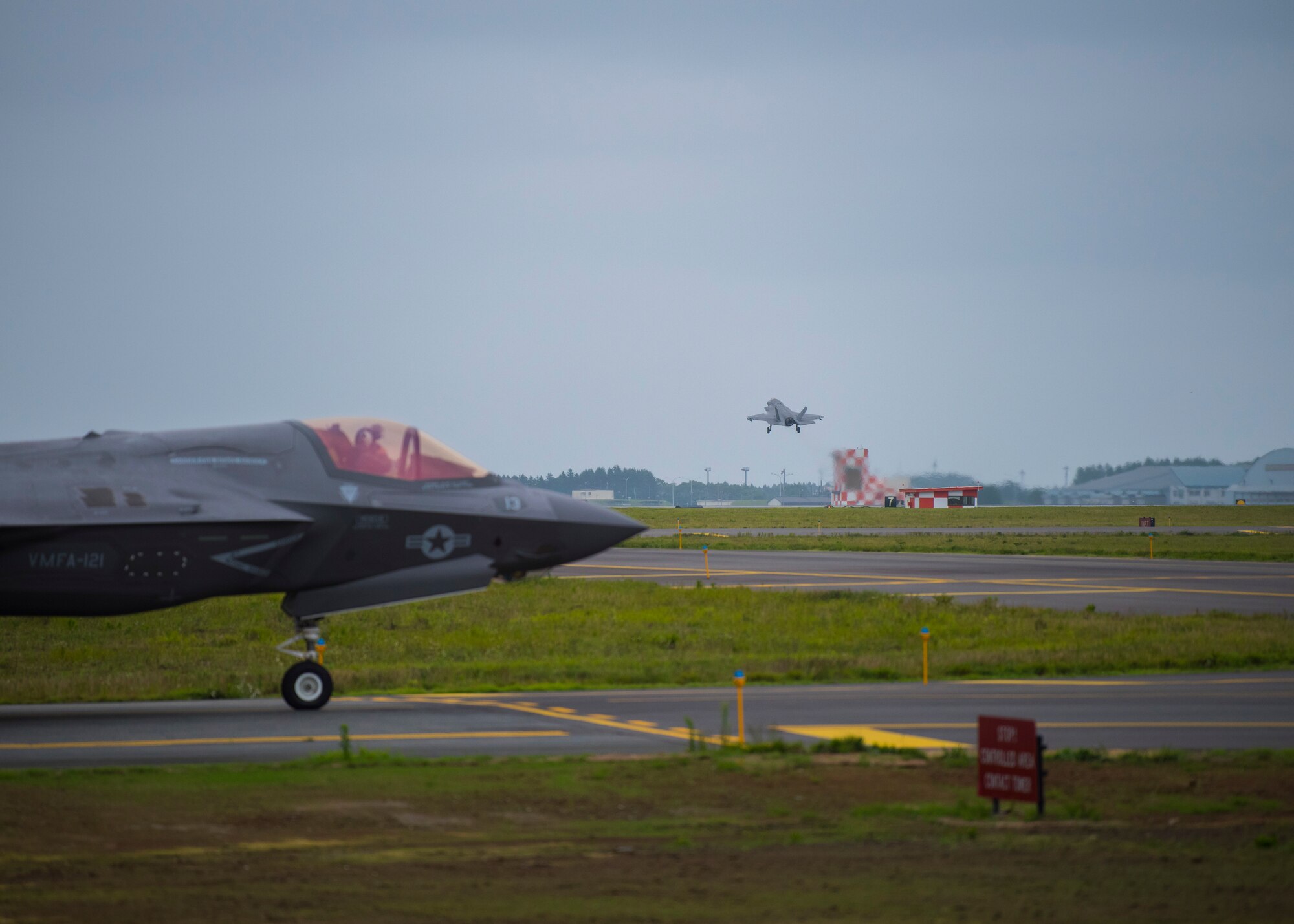 A fighter jet taxis from the left as another takes off from a runway.