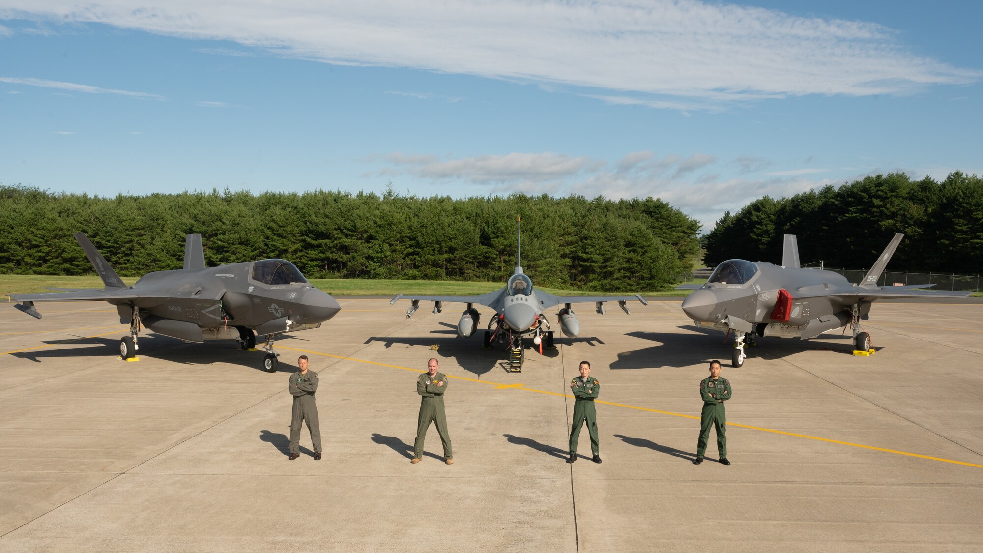 Four men in uniform stand in front of three fighter jets.
