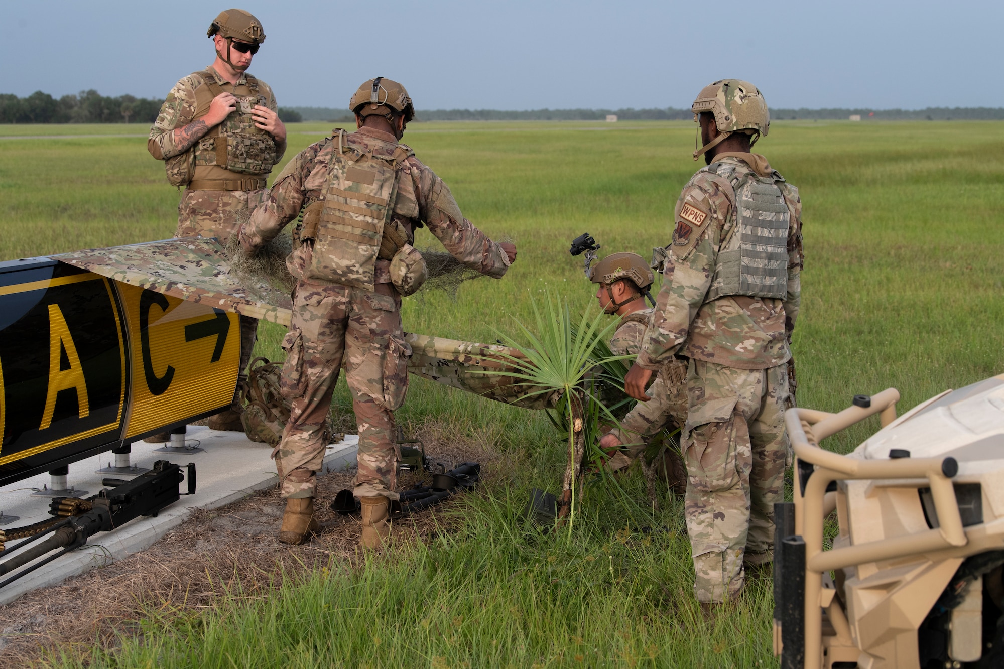 A photo of four Airmen crouched next to a makeshift shelter in the grass.