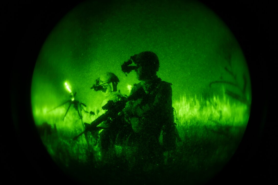 A photo of two Airmen kneeling in the grass. Photo is taken with a night vision lens, so the photo is green.