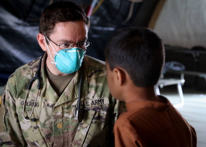 A doctor in an army uniform looks at a child.