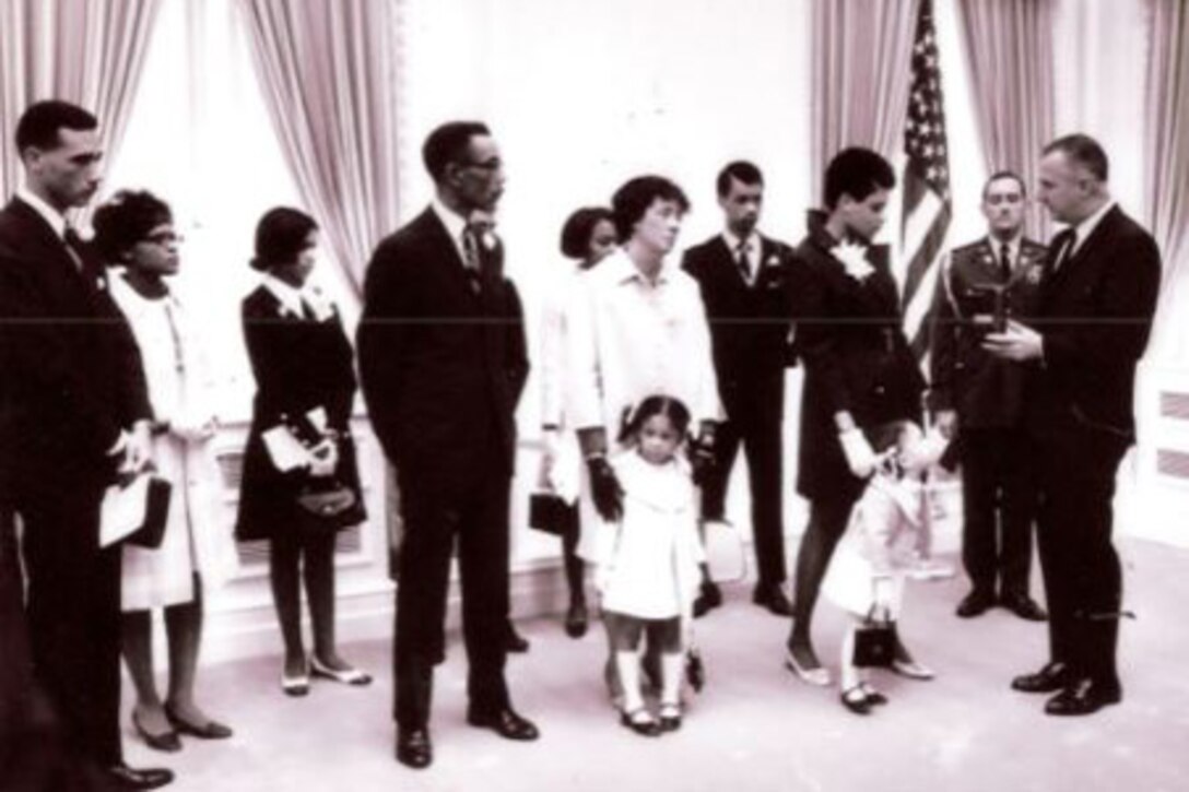 Members of a family stand beside two men, one of whom holds a small case.