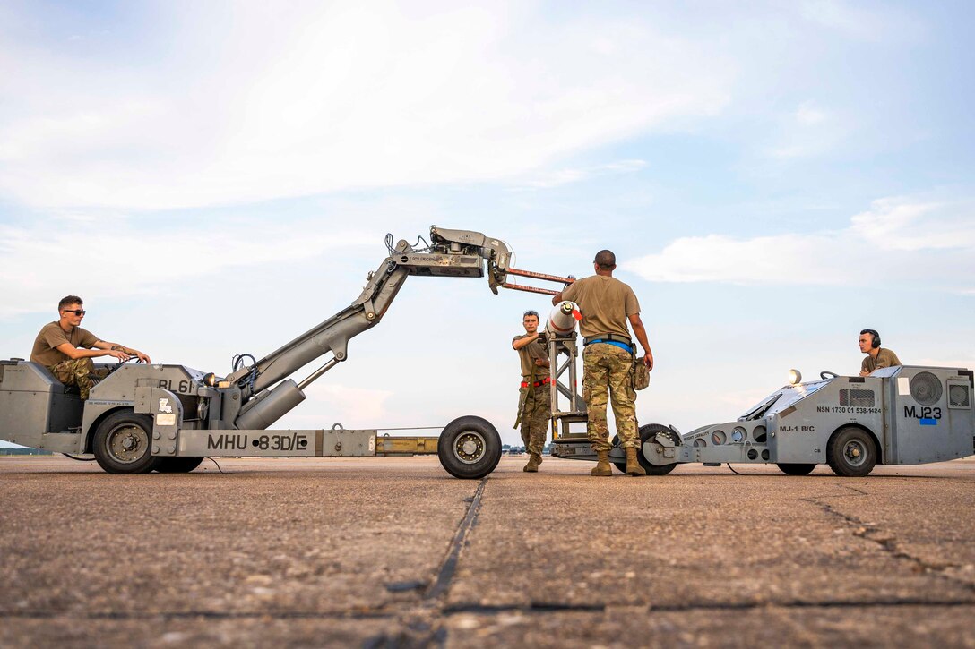 Two airmen operate military equipment as two others stand in between.