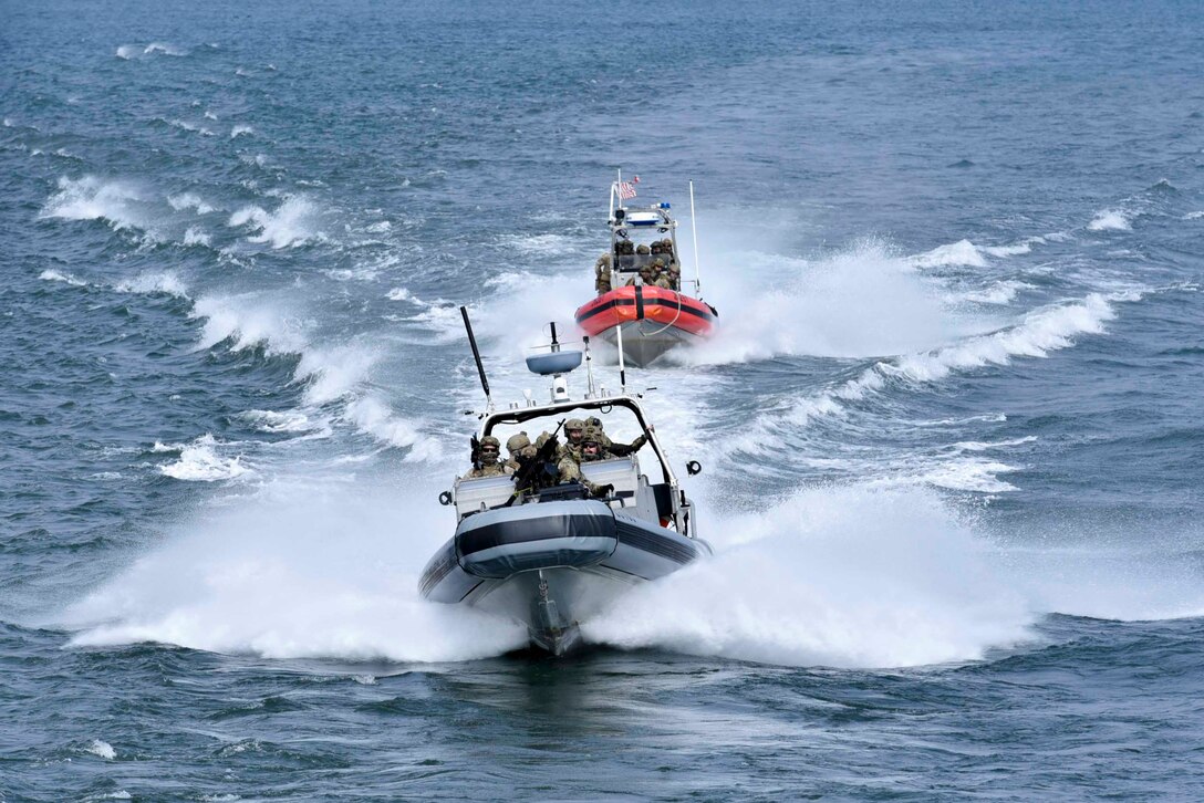 Coast Guardsmen travel through waters in two small boats.