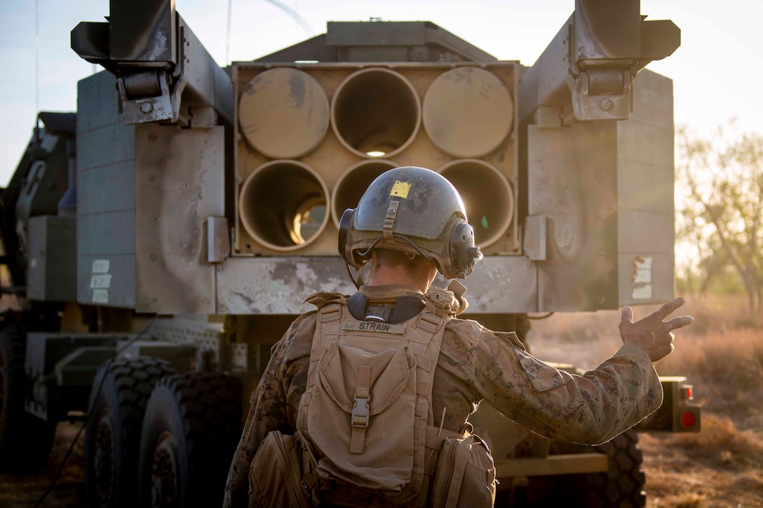 A Marine stands behind a guided multiple launch rocket system.