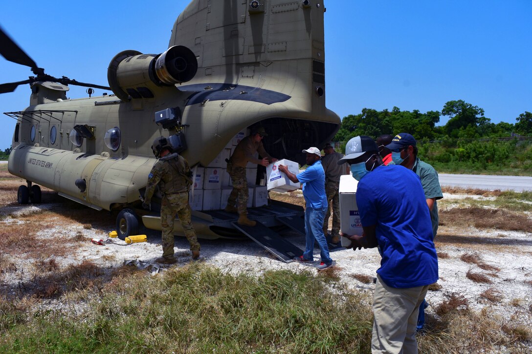 Service members and civilians unload boxes from the back of a helicopter.