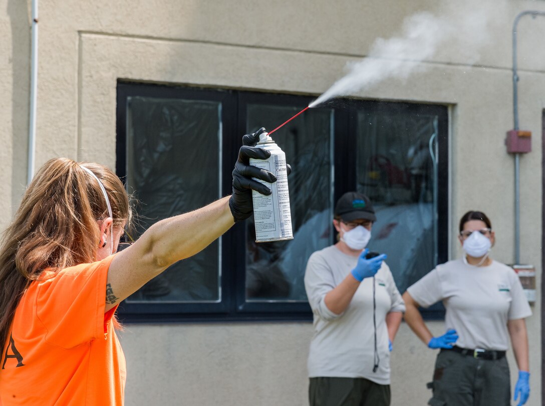 Emily Wallis, U.S. Department of Agriculture biological science laboratory technician, releases a six-second application of 10% d-Phenothrin insecticide at Dover Air Force Base, Delaware, Aug. 19, 2021. Melissa Benzinger McGlynn, USDA biological science laboratory technician, timed the release, as Lianmarie Colon Torres, USDA plant health safeguard specialist, recorded and formulated an optimal application time to use in Spotted Lanternfly experiments. (U.S. Air Force photo by Roland Balik)