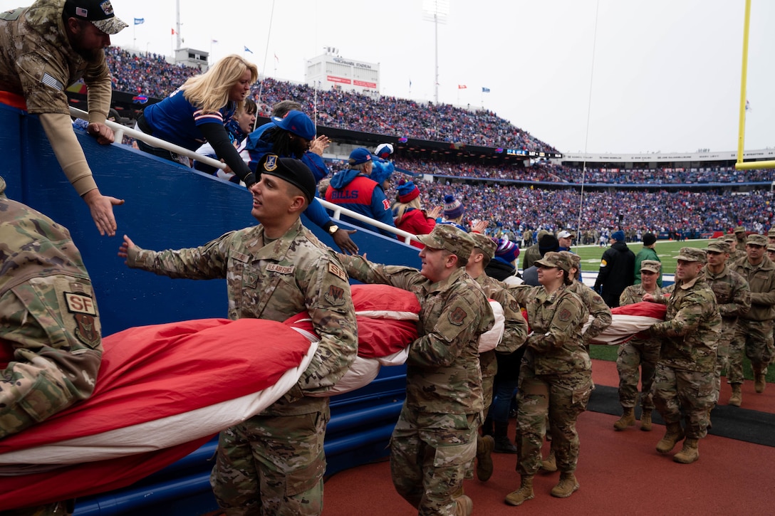 Service members shake hands with football fans as they walk off a playing field.