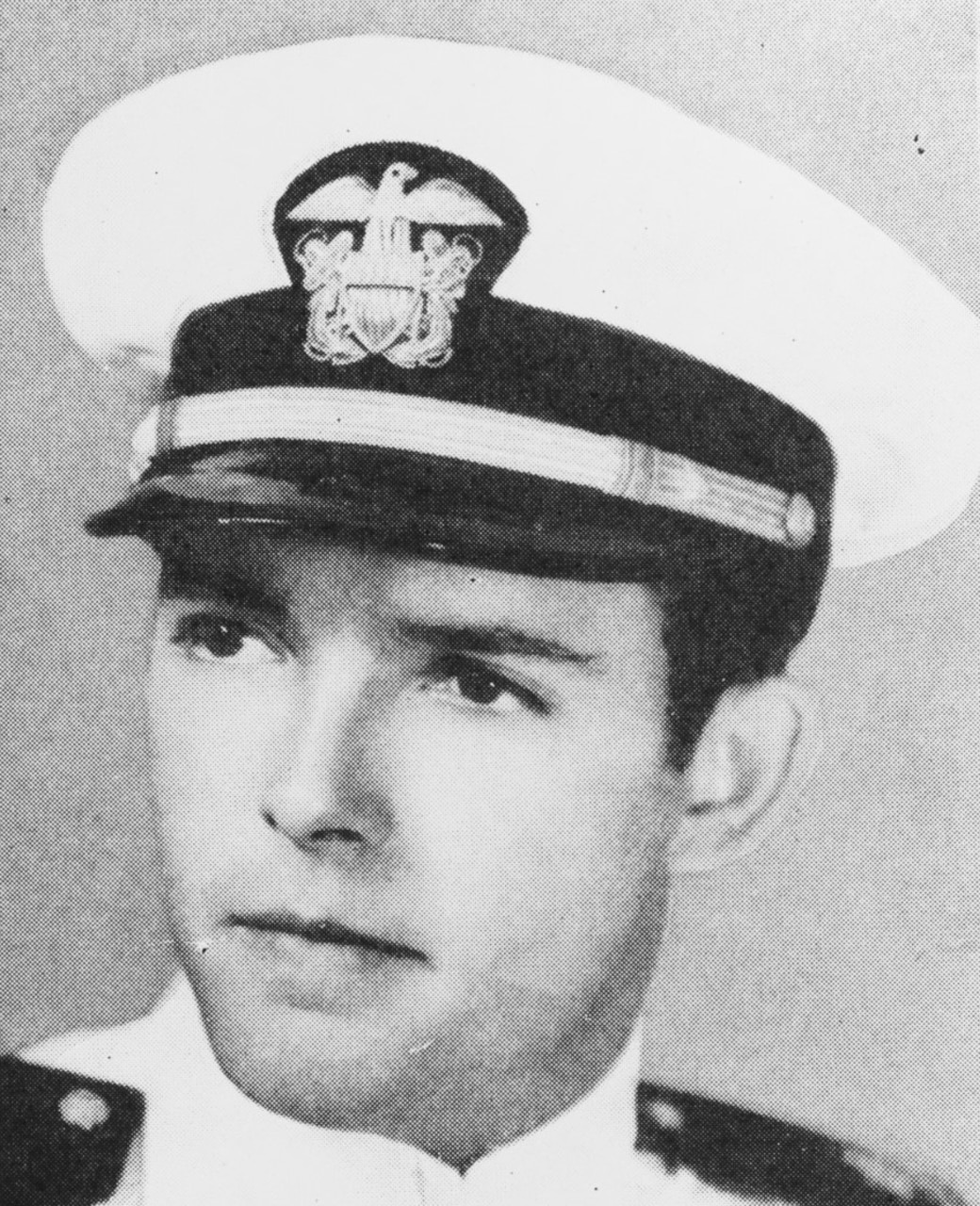 A man wearing a Navy dress cap poses for a photo.