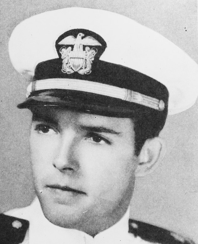 A man wearing a Navy dress cap poses for a photo.