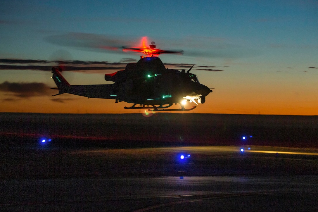 A helicopter prepares to land in the dark illuminated by blue, red and green lights.