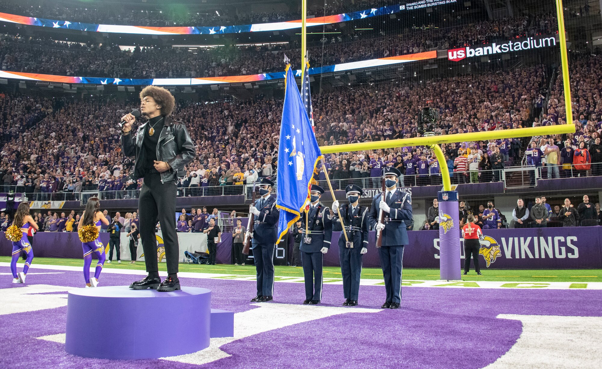 Four honor guardsmen stand in front of a large stadium