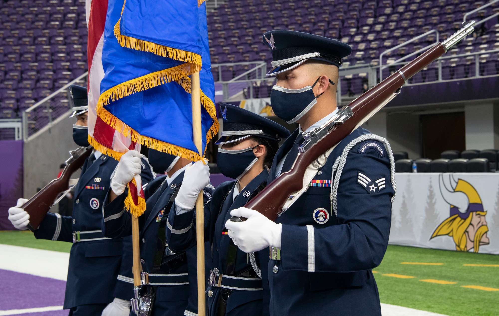 Four honor guardsmen stand in front of an empty stadium