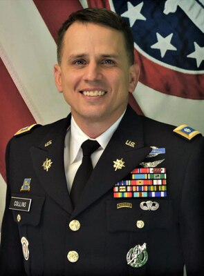 man in u.s. army uniform standing in front of flags.