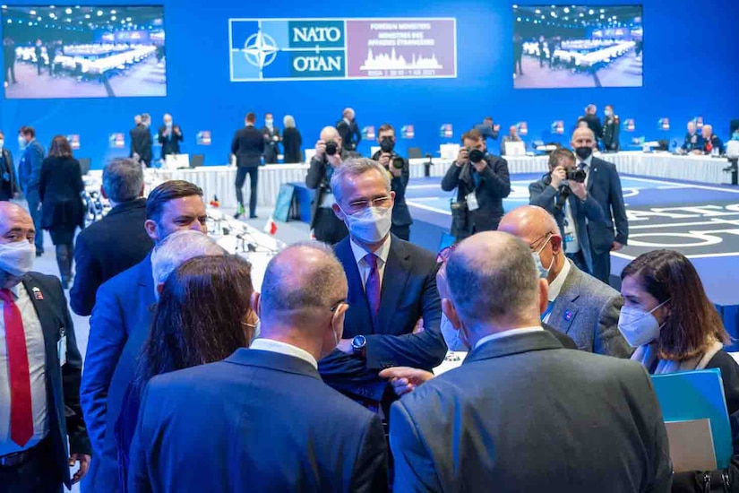 Five men and two women stand in a circle facing one another; the group is inside a large conference room.