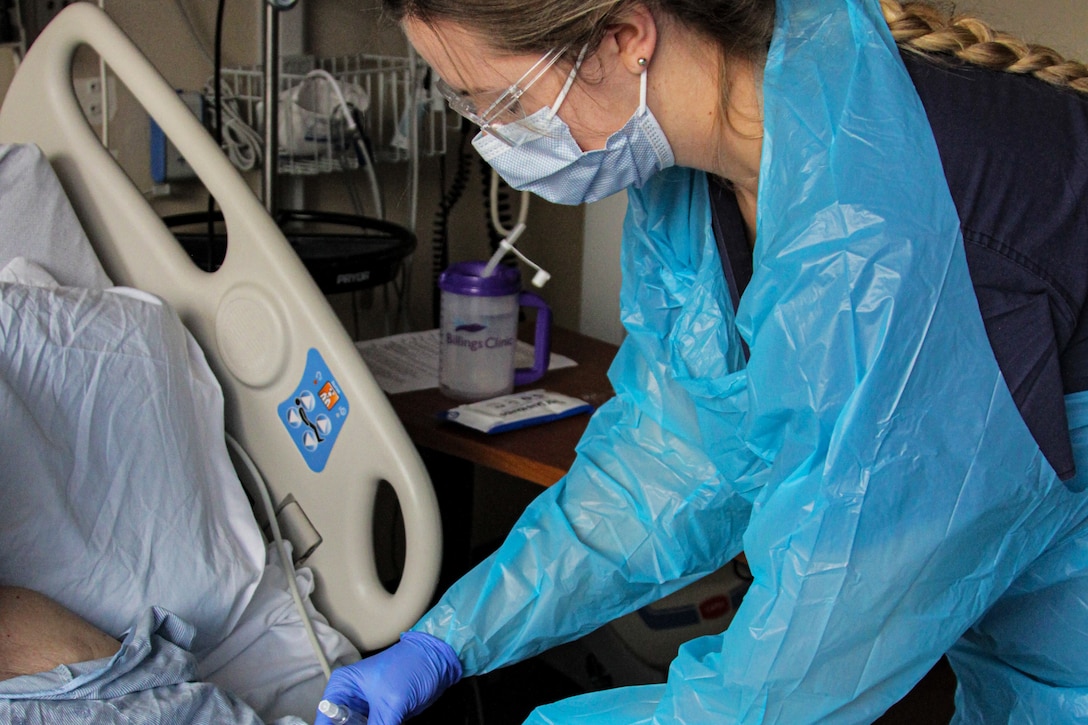 A sailor flushes the IV tubes for a patient in a hospital bed.