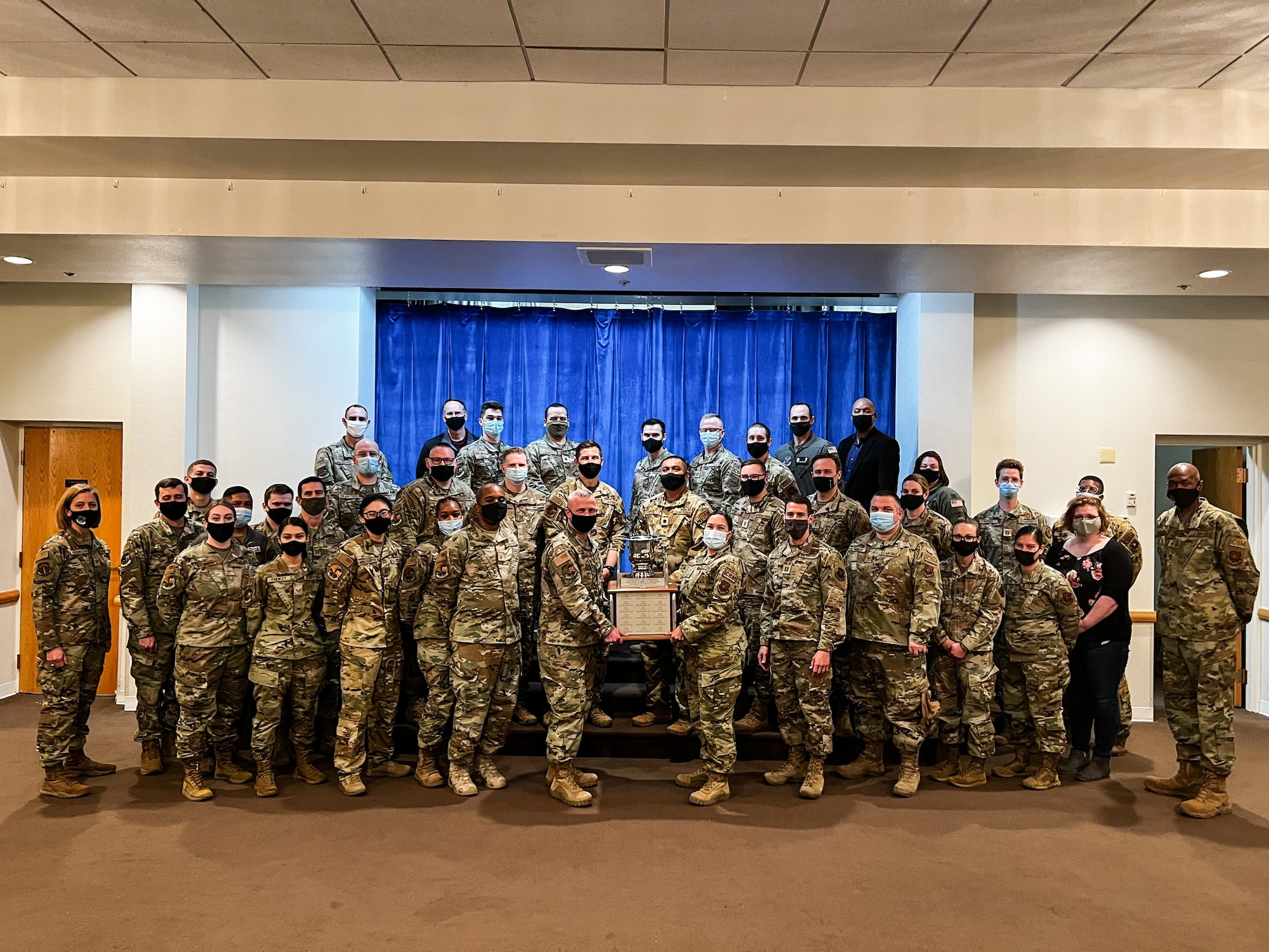 The Airmen of the 90th Operations Support Squadron pose for a group photo while holding the Col. Lowell F. McAdoo Award for the most outstanding intercontinental ballistic missile operations for 2020 on F.E. Warren Air Force Base, Wyoming, Nov. 23. 2021. The squadron earned this by executing 364 nuclear orders and 8,700 alert hours during the pandemic. Also, they organized and led the Air Force's first and only drive-in airshow with 4,500 people in attendance while ensuring the health and safety of its spectators. (U.S. Air Force photo by Joseph Coslett)