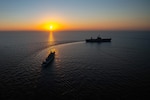 Two ships transit a body of water under a sunlit sky.