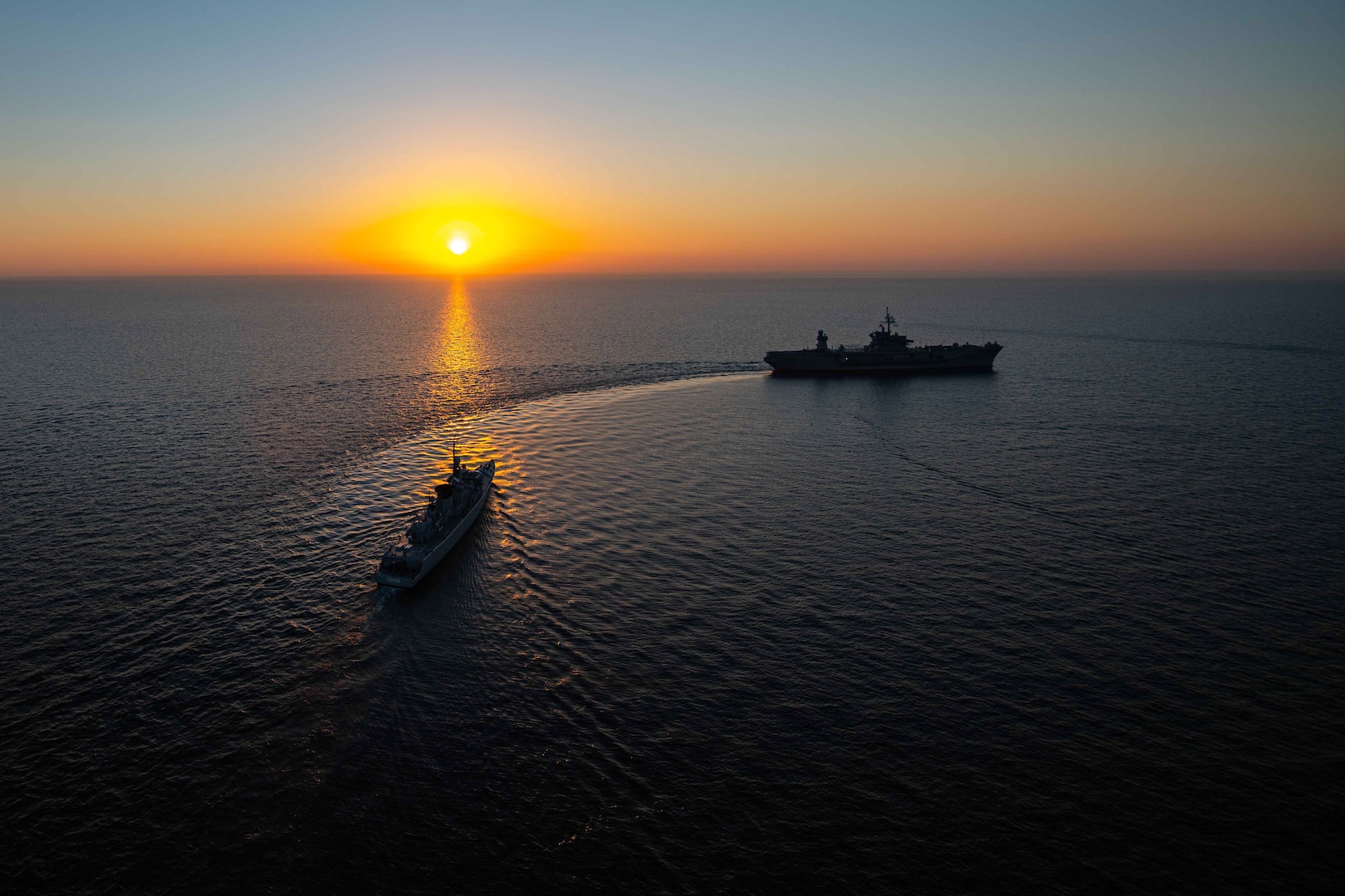 Two ships transit a body of water under a sunlit sky.