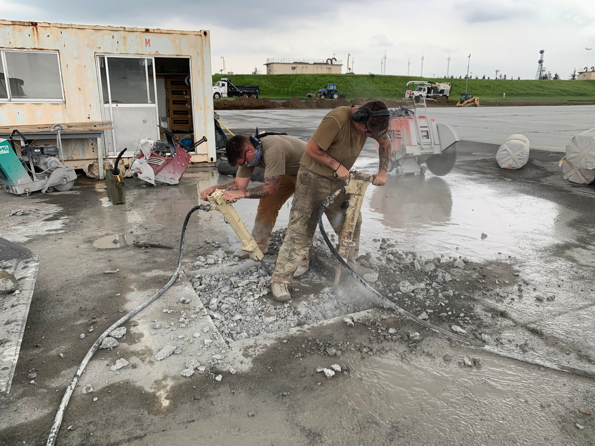Two construction workers use jackhammers to carve out a square hole in a runway