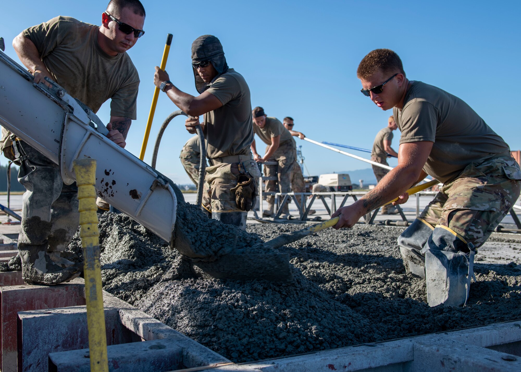 several construction Airmen rake fresh concrete into shape