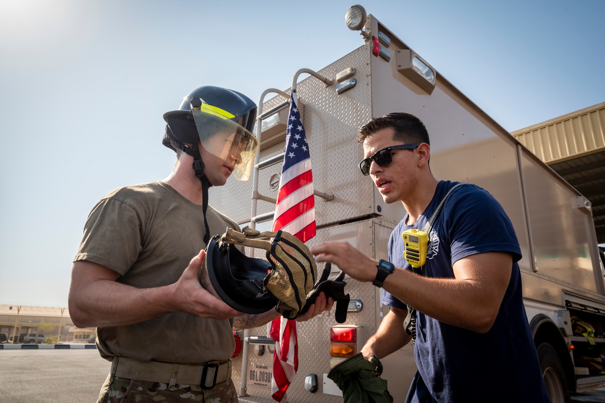 U.S. Air Force Airman 1st Class Kelvis Yera-Alonso, right, 379th Expeditionary Civil Engineer Squadron firefighter, explains how to don a firefighting mask to Senior Airman Jakob Poleno, left, 379th ECES force protection, at Al Udeid Air Base, Qatar, Nov. 27, 2021.