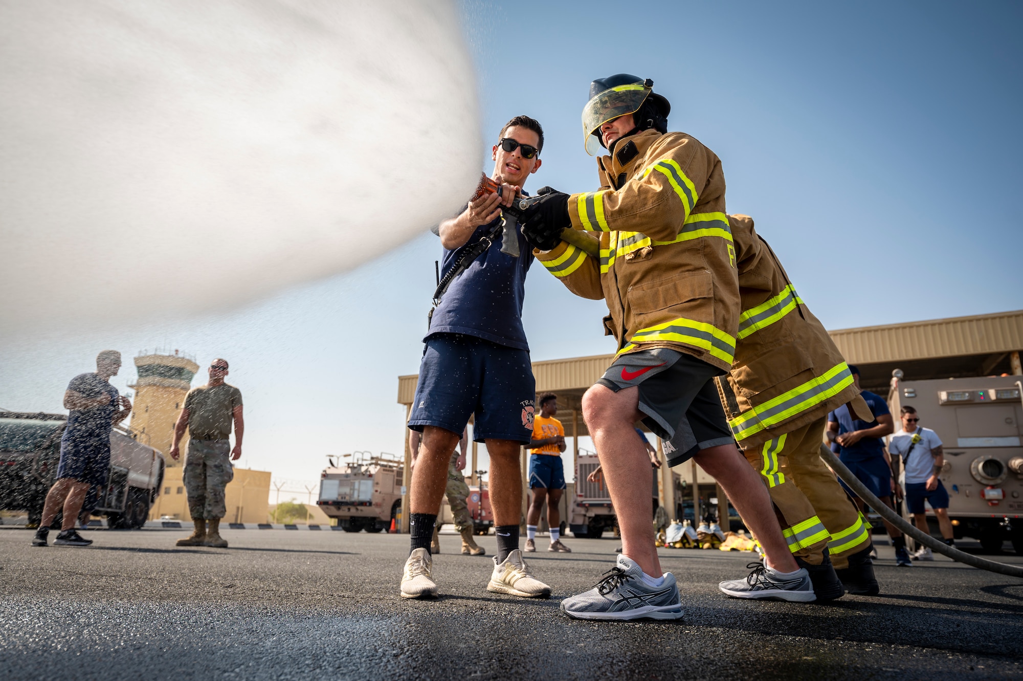 U.S. Air Force Airman 1st Class Kelvis Yera-Alonso, left, 379th Expeditionary Civil Engineer Squadron firefighter, instructs Staff Sgt. Joshua Yewcic, right, 379th ECES force protection, how to handle a firehose at Al Udeid Air Base, Qatar, Nov. 27, 2021.