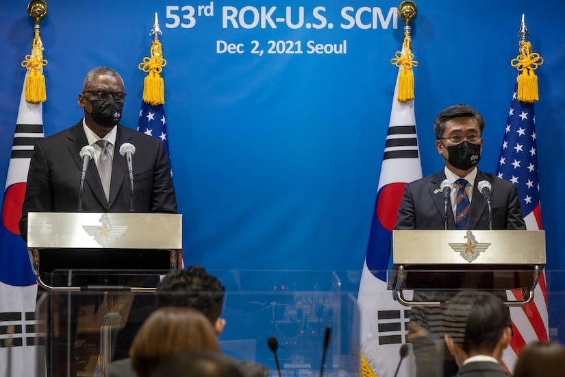 Two men stand at two different lecterns in front of a crowd.