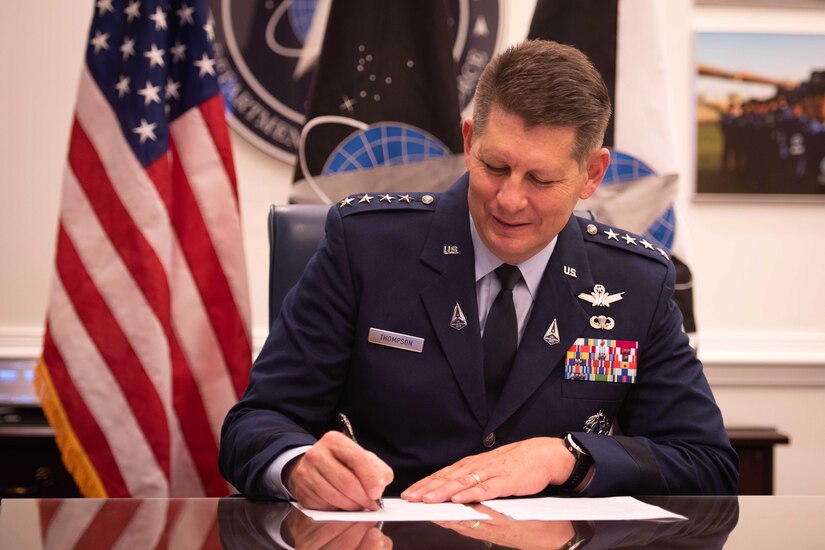 An officer sits at a desk and signs a sheet of paper.