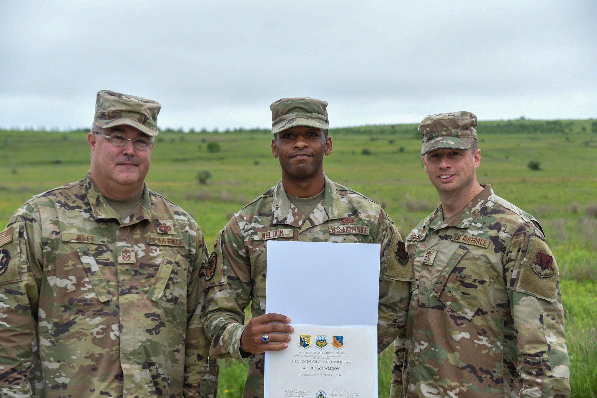 Three men in military uniform pose for a photo outside.