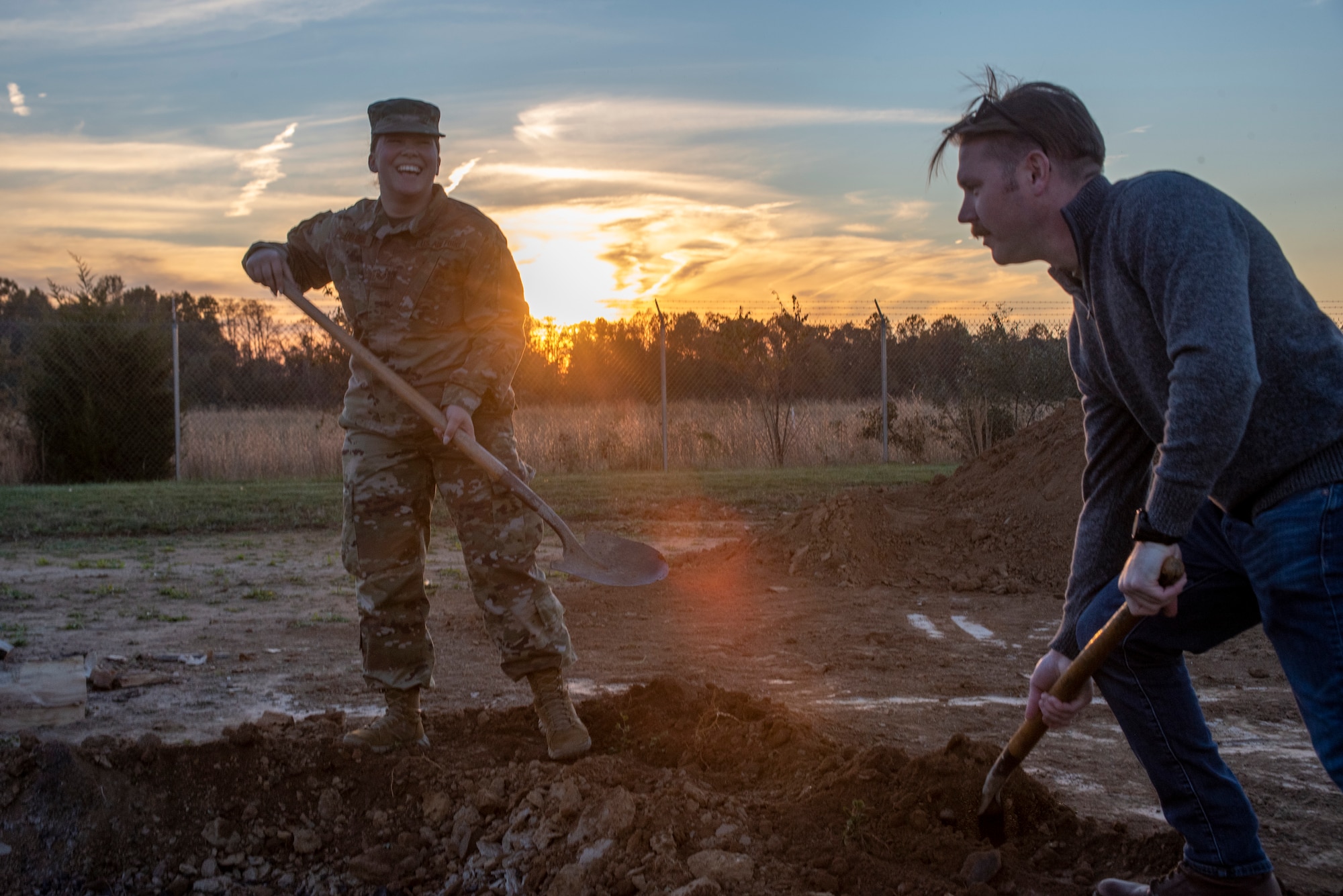 A woman in uniform helps a man in civilian attire shovel.