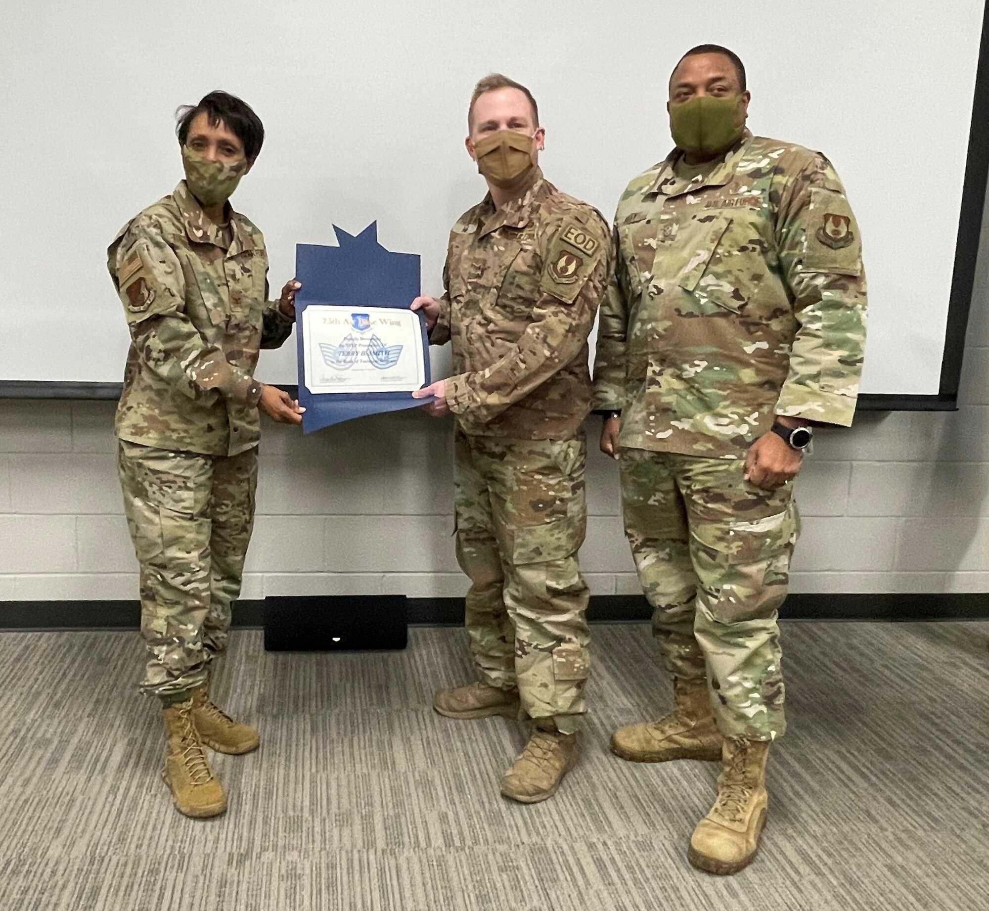 Col. Carroll and Chief Master Sgt. Riley hold up the new technical sergeant rank to Tech. Sgt. Smith's chest.