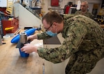 Lt. Joshua Kish, Engineering Duty Officer Reservist assigned to SurgeMain Atlanta, joins two 3D printed hull portions together with epoxy. This process allows the two hull forms that were 3D printed to join, creating a section of the unmanned underwater vehicle prototype.