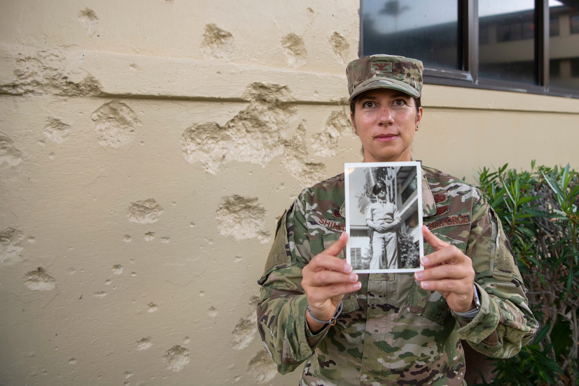 Col. Athanasia Shinas holds a photo of her grandfather, Private Ralph Yeager, in front of the bullet- and shrapnel-marked facade of the Pacific Air Forces building in Hawaii.