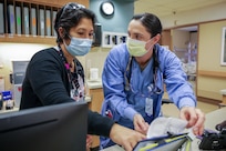 Two women wearing facemasks talk while looking at notes in an office.