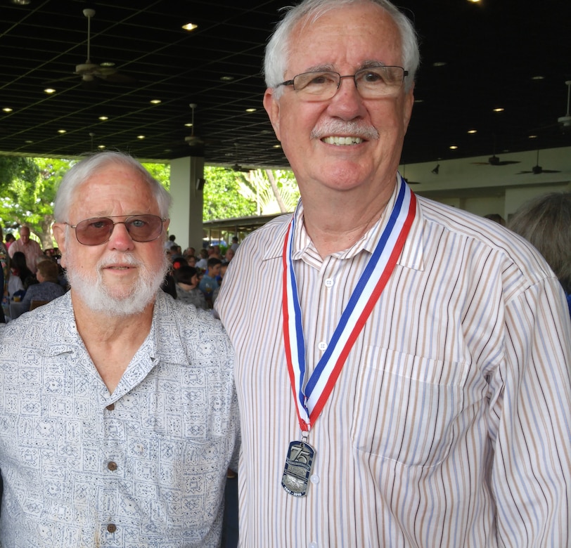 Two older men stand beside each other to pose for a photo.