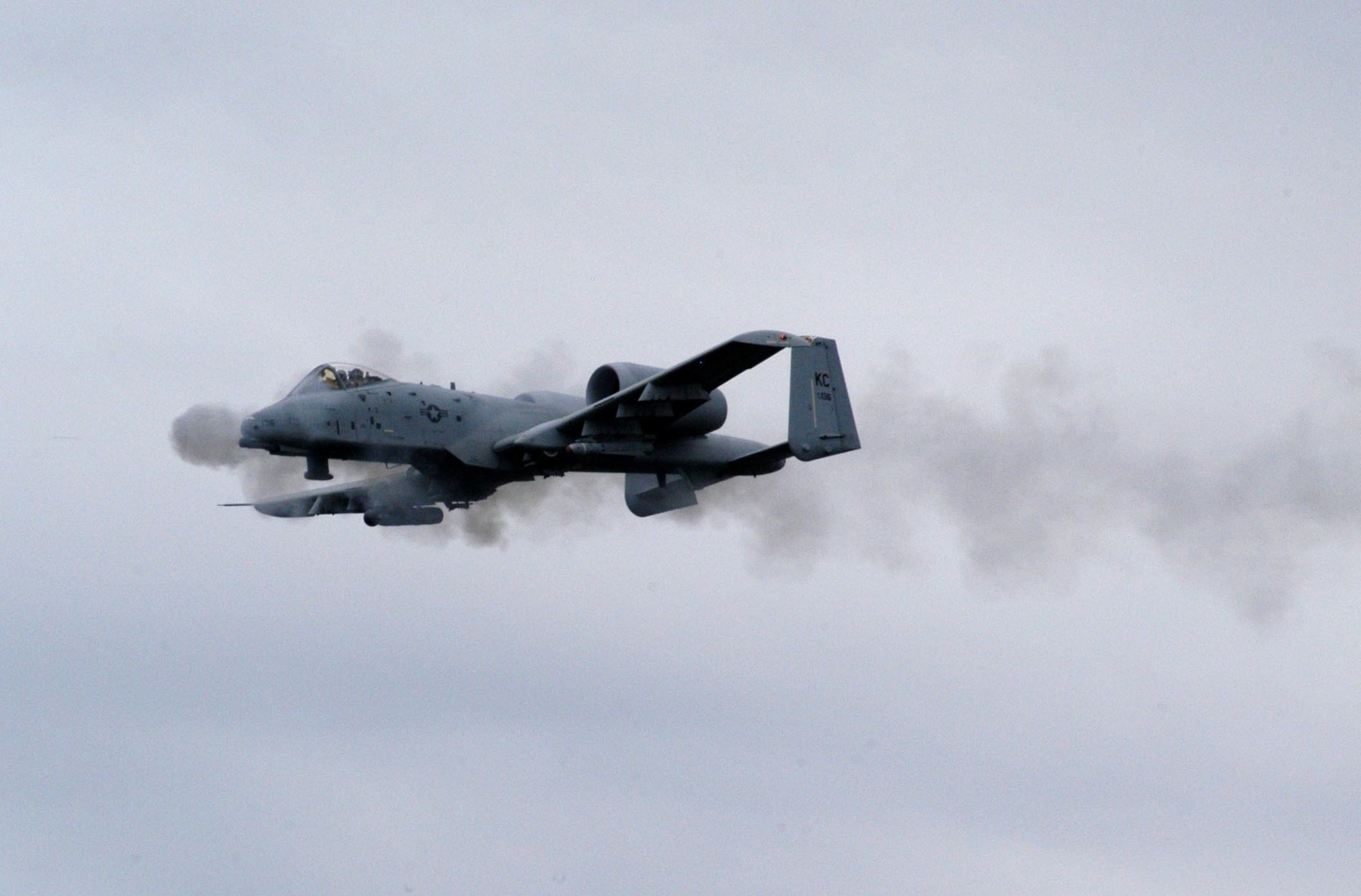 An A-10 Thunderbolt II flies from right to left and trails smoke from its nose gun as it fires.