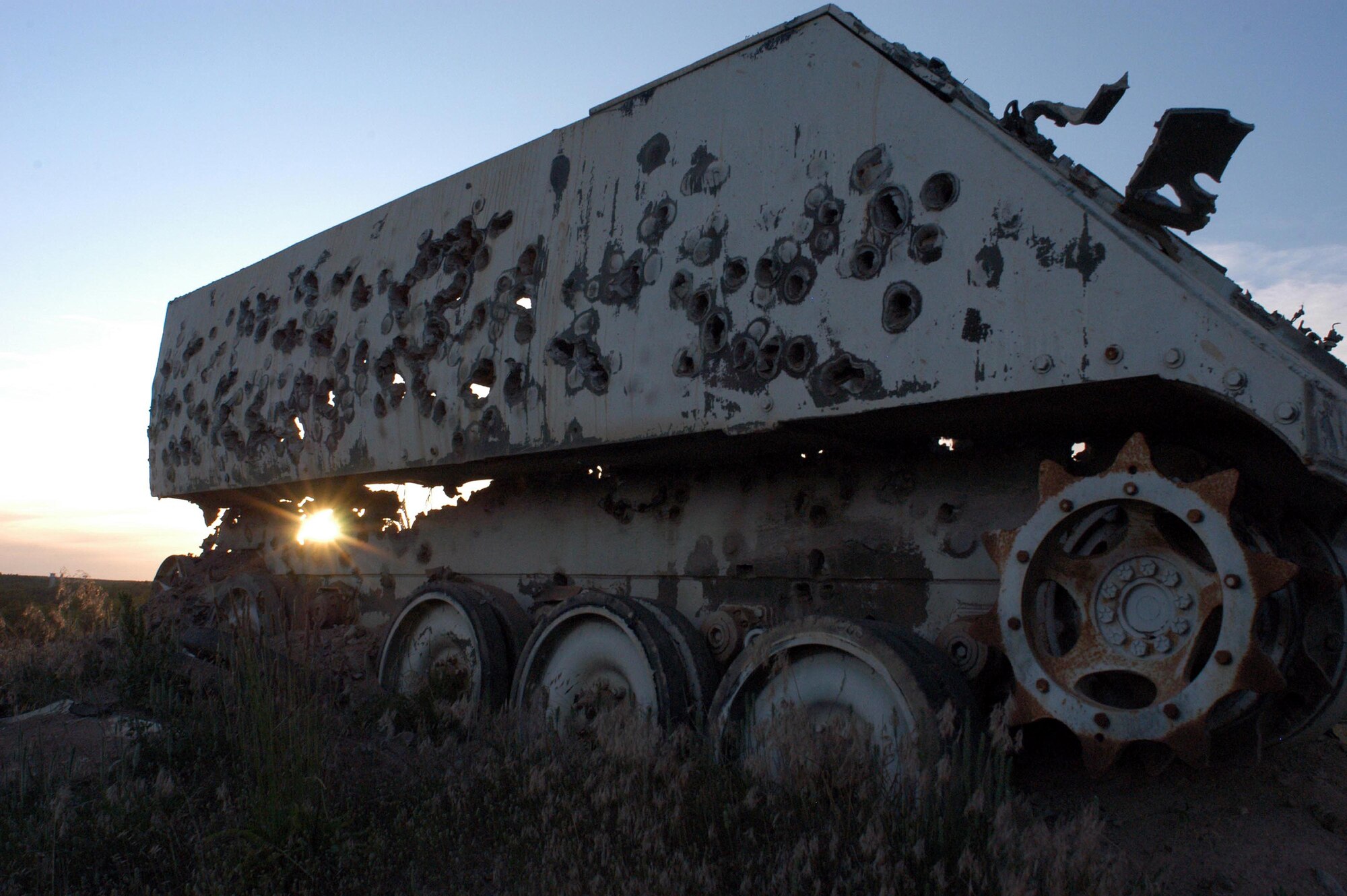 The setting sun peeks through an armored personnel carrier riddled with holes from A-10 30mm training rounds.