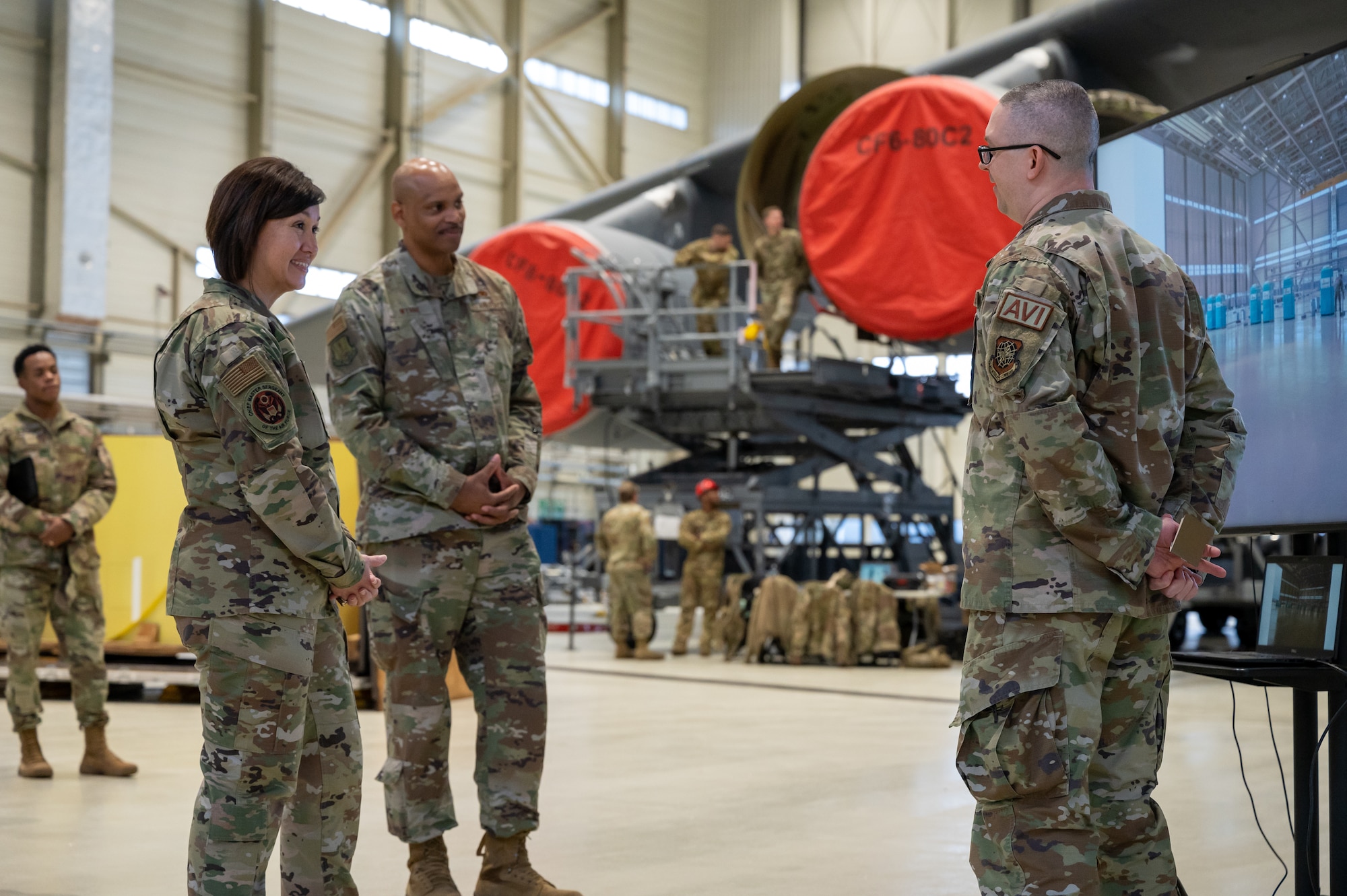 Military members standing in a hangar with an aircraft.