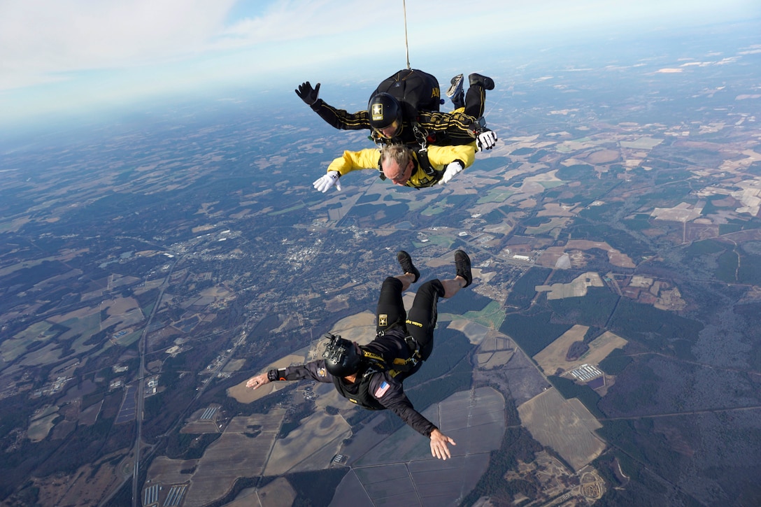 A skydiver soars beneath two tandem divers in the sky before their parachutes are opened.